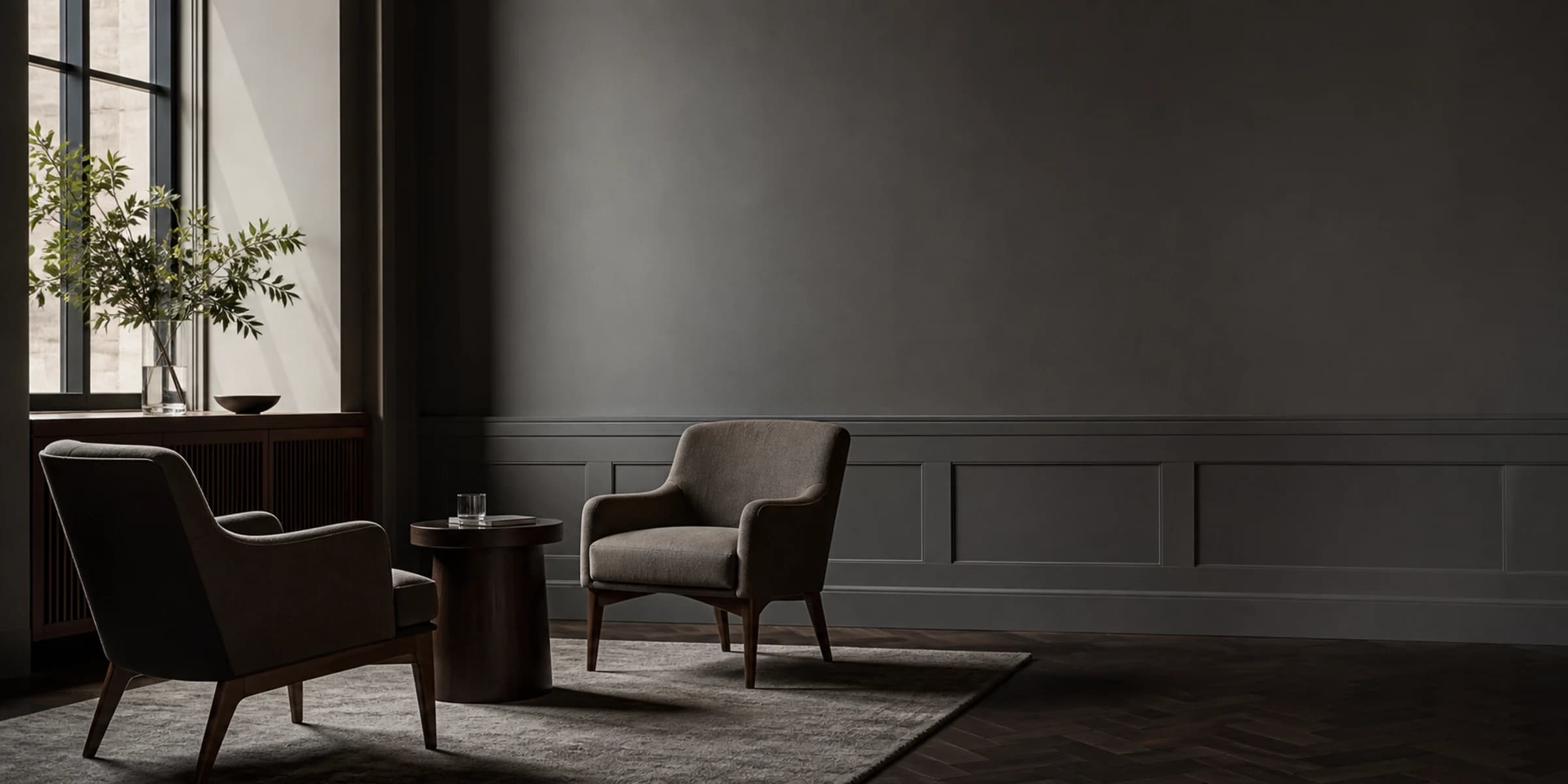 Two empty chairs angled toward a small table in low window light.